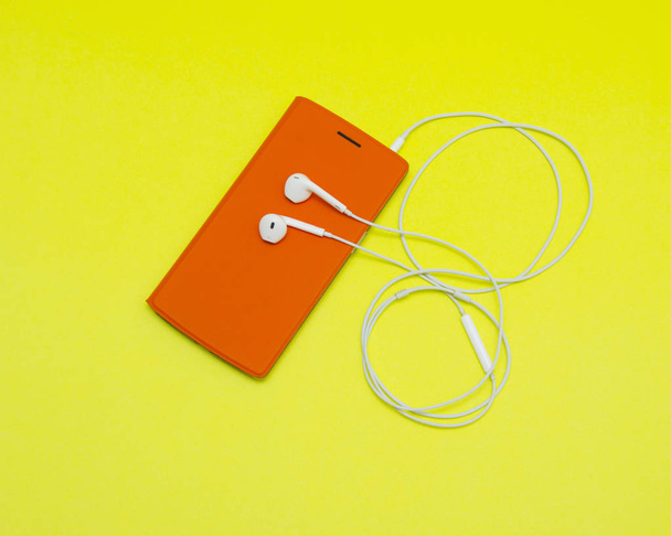 Smartphone με ακουστικά σε κίτρινο φόντο  - Φωτογραφία, εικόνα
