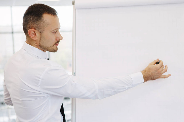 Teamwork of office staff. Businessman coach in a white shirt and tie, standing near the flipchart, explains the schedule of tasks for the future. Business training. Personal growth. - Fotoğraf, Görsel