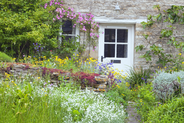Portes en bois blanc dans un charmant chalet de campagne anglais avec jardin devant plein de fleurs en fleurs, rose rose, figuier escaladant le mur de pierre
 . - Photo, image