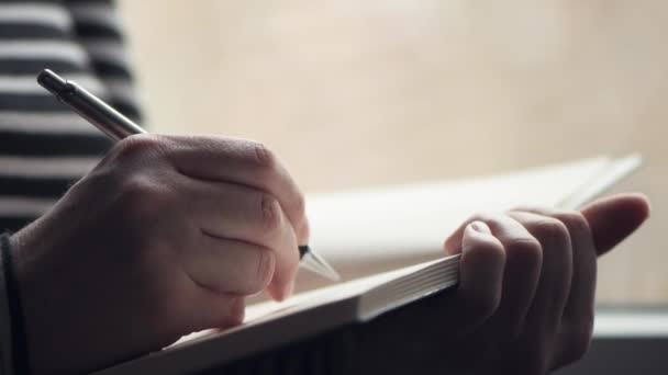 Woman writing diary by the window of her living room, close up with selective focus - Filmagem, Vídeo