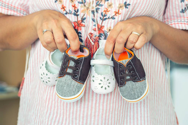 Pregnant woman holding little baby girl and boy shoes - Фото, зображення