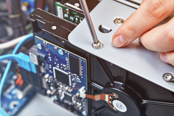 Repairman is untightening the screw of the HDD of the unassembled computer system unit, close up. - Φωτογραφία, εικόνα