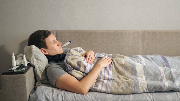 Sick man with thermometer lying on sofa - 写真・画像