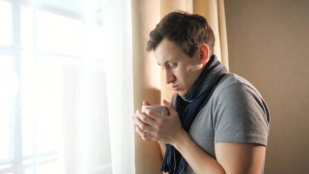 Άρρωστος άνθρωπος με ζεστό ρόφημα κοντά σε παράθυρο - Φωτογραφία, εικόνα