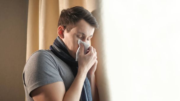 Άρρωστος άνθρωπος φυσούν τη μύτη κοντά σε παράθυρο - Φωτογραφία, εικόνα