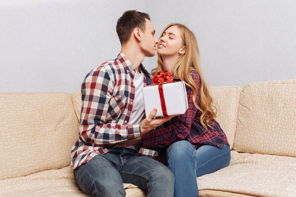 Young couple, a man gives a woman a gift, sitting on the couch at home, the concept of Valentine's Day - Foto, afbeelding