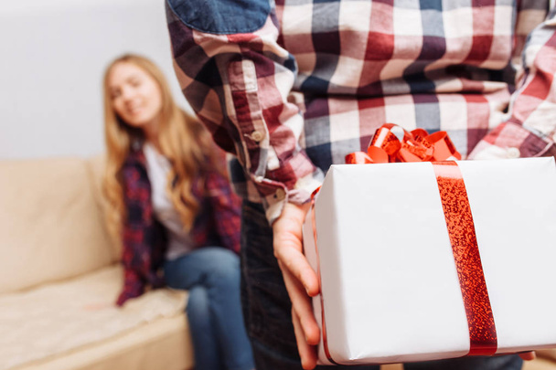 photo of male hands hiding with a gift behind the back, happy woman on blurred background - Photo, Image