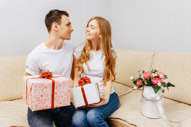 young couple, man and woman give each other gifts while sitting at home on the couch - Foto, imagen