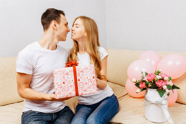 Couple in love, man gives a gift, woman sits at home on the sofa - Valokuva, kuva
