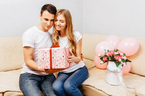 Couple in love, man gives a gift, woman sits at home on the sofa - Photo, Image