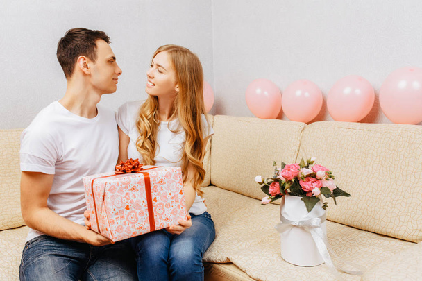 Couple in love, man gives a gift, woman sits at home on the sofa - Valokuva, kuva