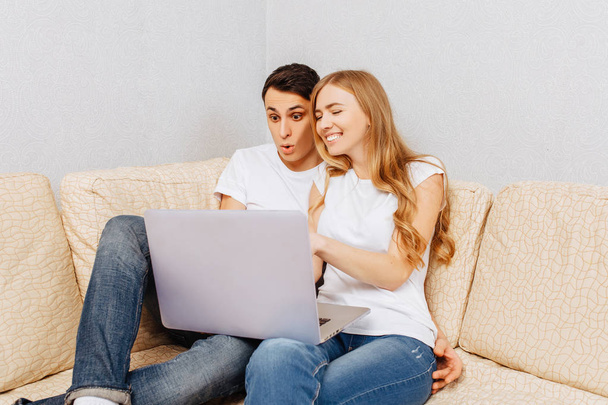 Happy young couple, man and woman, using laptop, hugging and smiling, sitting at home on the couch - Fotografie, Obrázek