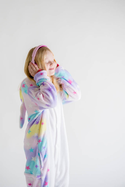 la moda moderna - la muchacha hermosa rubia escucha la música con los auriculares sobre el fondo blanco en el pijama kigurumi
 - Foto, imagen