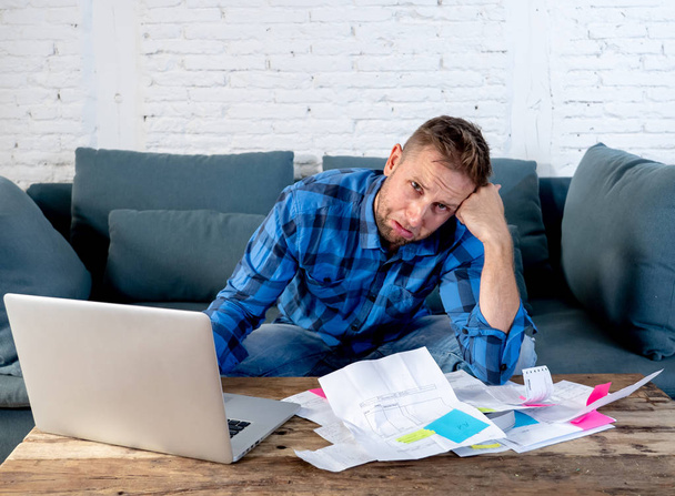 Worried and stressed man calculating bills tax expenses and counting home and business finances sitting on the couch at home in paying off debts and domestic bills and financial problems concept. - 写真・画像