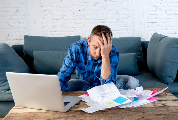 Worried and stressed man calculating bills tax expenses and counting home and business finances sitting on the couch at home in paying off debts and domestic bills and financial problems concept. - Фото, изображение