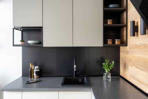 Elegantie interieurconcept. Foto van zwarte en witte moderne Keukenmeubels met plank en verschillende dingen op tafel - Foto, afbeelding
