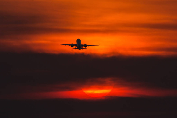 Avion décollant au coucher du soleil près du soleil avec un beau nuage rouge en arrière-plan
 - Photo, image