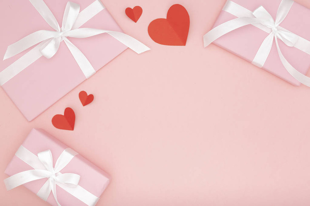 Valentine den myšlenka složení: růžové krabičky s bílou stuhou a malé červené srdce na papír korálové pozadí. Pohled shora. Láska den koncept ploché rozložení - Fotografie, Obrázek