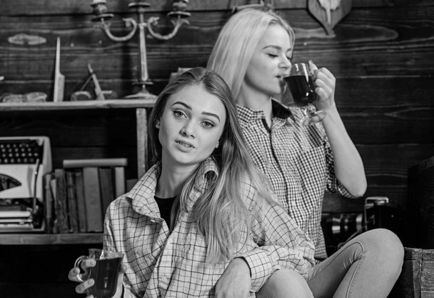 Friends on calm faces in plaid clothes relaxing. Girls relaxing and drinking mulled wine. Friends in casual outfits enjoy warm atmosphere, wooden interior. Holiday and vacation concept - Foto, immagini