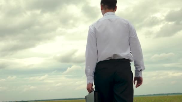 Agronom v obleku kontroluje oblast pro pěstování obilí. Podnikatel v bílou košili jde s černou aktovkou dokumentů v ruce proti pozadí temné mraky - Záběry, video