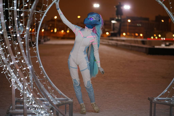 estranha anime cabeça menina olhando como uma grande boneca vestindo macacão futurista andando no parque da cidade de inverno com luzes
 - Foto, Imagem
