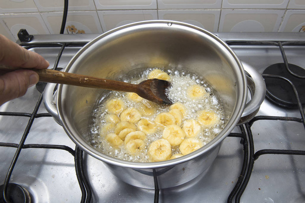 banana doce sendo cozida em uma panela de aço inoxidável em um xarope de açúcar
 - Foto, Imagem
