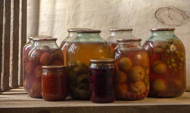Several cans of compote on a wooden shelf in a dark basement Close up - Zdjęcie, obraz