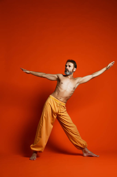 Fitness senior man doing exercise yoga asana leg isolated on a orange background - Foto, afbeelding