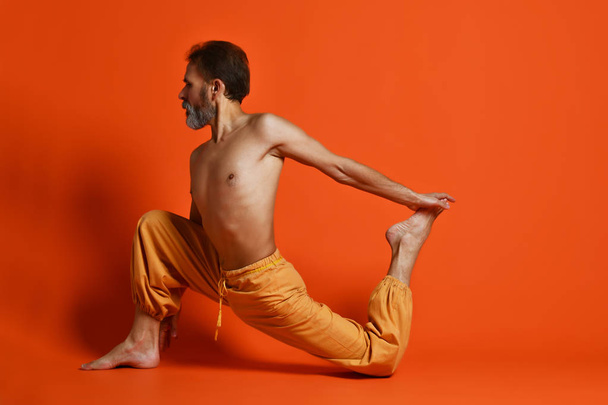 Viejo practicando yoga haciendo ejercicios de estiramiento sobre fondo naranja
 - Foto, imagen