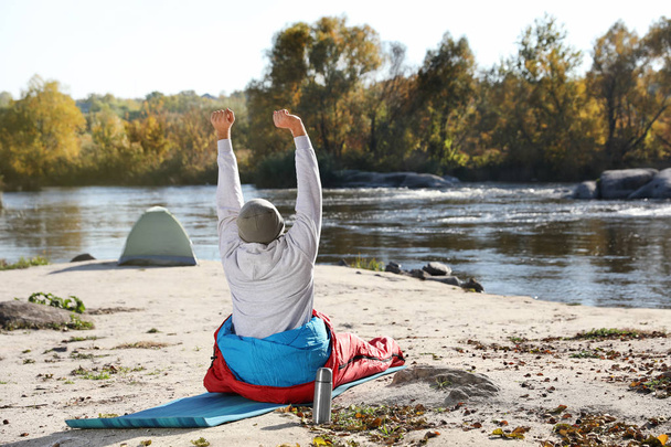 Male camper stretching in sleeping bag on wild beach. Space for text - Photo, Image