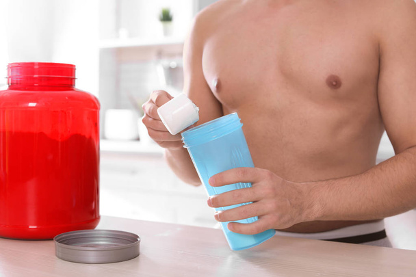 Young shirtless man preparing protein shake at table in kitchen, closeup - Photo, image