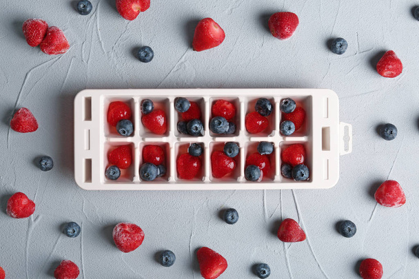 Flat lay composition with ice cube tray and berries on grey background - Foto, immagini