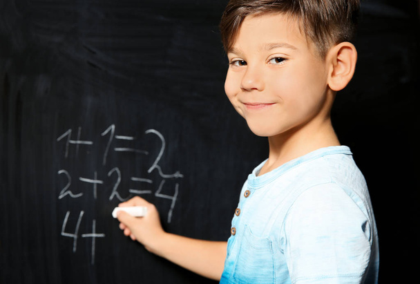 Little child writing letters and doing math on green blackboard - 写真・画像