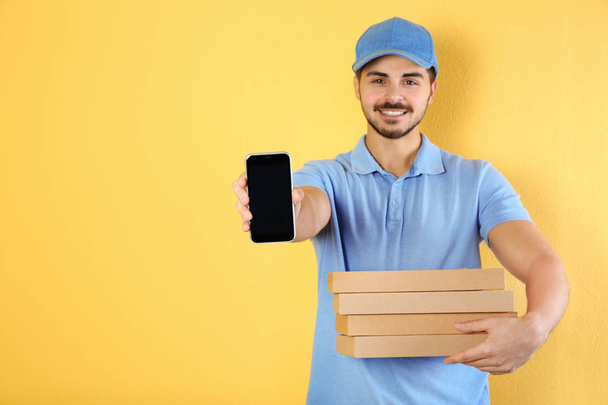 Young man holding pizza boxes and smartphone on on color background, mockup for design. Online food delivery - Fotó, kép