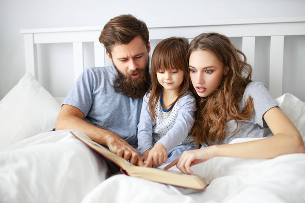 happy family mother, father and  father child daughter read a book, a fairy tale in be - Foto, afbeelding