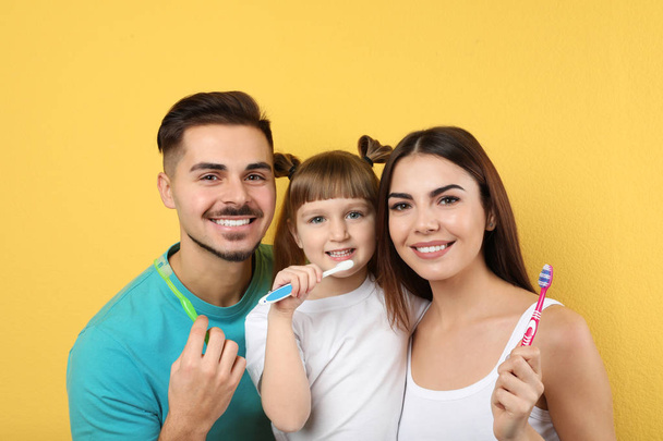 Little girl and her parents brushing teeth together on color background - 写真・画像