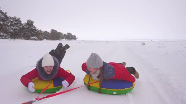 τα παιδιά με κόκκινα σακάκια χειμώνα βόλτα μέσα από το χιόνι σχετικά με έναν σωλήνα φουσκωτά χιονιού και έλκηθρο. Αθλητισμός κορίτσια Χαλαρώστε στο χειμερινό πάρκο για τις διακοπές των Χριστουγέννων. Αργή κίνηση - Πλάνα, βίντεο