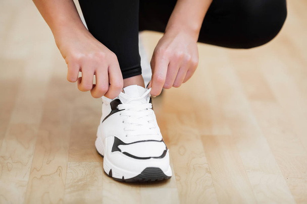 Aktywności fizycznej. Zbliżenie: Dziewczyna wiązania sznurowadeł na buty sportowe w siłowni - Zdjęcie, obraz