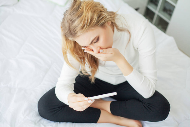 Pozitivní těhotenský test. Mladá žena cítit depresivní a smutný po pohledu na výsledek těhotenského testu doma - Fotografie, Obrázek