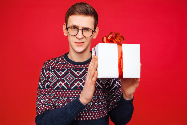 Curious man with glasses, a man holding a gift box, shaking it to find out what is inside the box - Fotó, kép