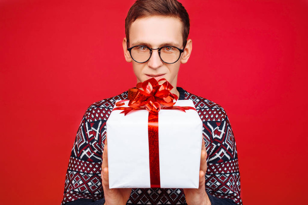 Curious man with glasses, a man holding a gift box, shaking it to find out what is inside the box - Foto, Bild
