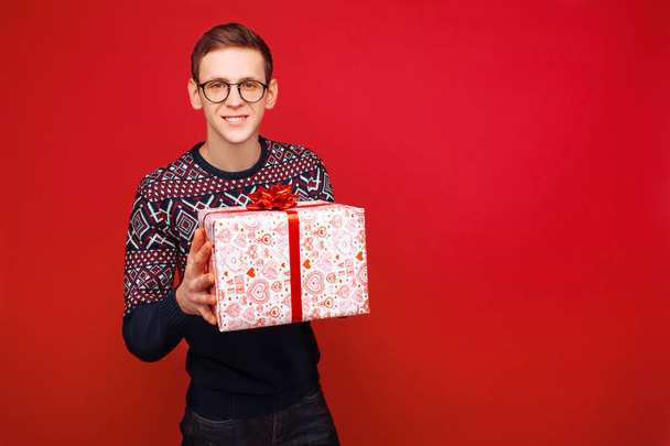 Man in glasses with a gift box in his hands on a red background - Foto, Imagen