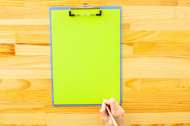 Mano de oficina sosteniendo una carpeta con un papel de color verde en el fondo de la mesa de madera. Copyspace. Lugar para el texto
 - Foto, imagen