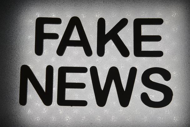 woord "nep nieuws" geschreven in houten letters en verlicht door de achtergrond van de achtergrondverlichting - Foto, afbeelding