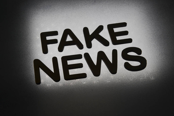 Wort "Fake News" in Holzbuchstaben geschrieben und durch Hintergrund im Gegenlicht beleuchtet - Foto, Bild