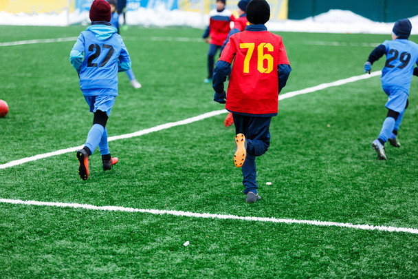 Jongens in rode en blauwe sportkleding speelt voetbal op groen grasveld. Jeugd voetbalspel. Kinderen sport concurrentie, kinderen spelen buiten, Winteractiviteiten, opleiding - Foto, afbeelding