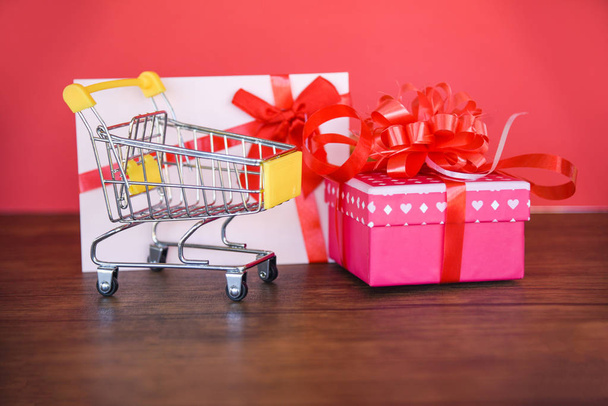 バレンタインの日のショッピングしギフト カード ギフト ボックス ショッピング カート/ピンクを呈するボックス メリー クリスマス休日幸せに赤いリボン弓ギフト カードに赤背景に - 新年ショッピング休暇 - 写真・画像