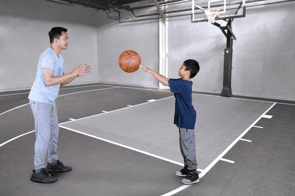Picture of little boy passing a ball to his father while doing basketball exercises in the court - Photo, Image
