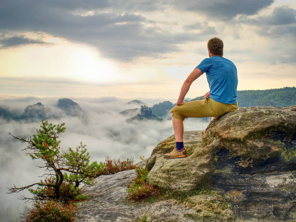 Hiker in middle of nowhere and thinking alone. Man sit on top of a sharp peak enjoying sunrise. - Photo, Image