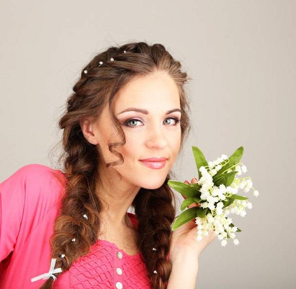 Young woman with beautiful hairstyle and flowers, on grey background - Foto, imagen